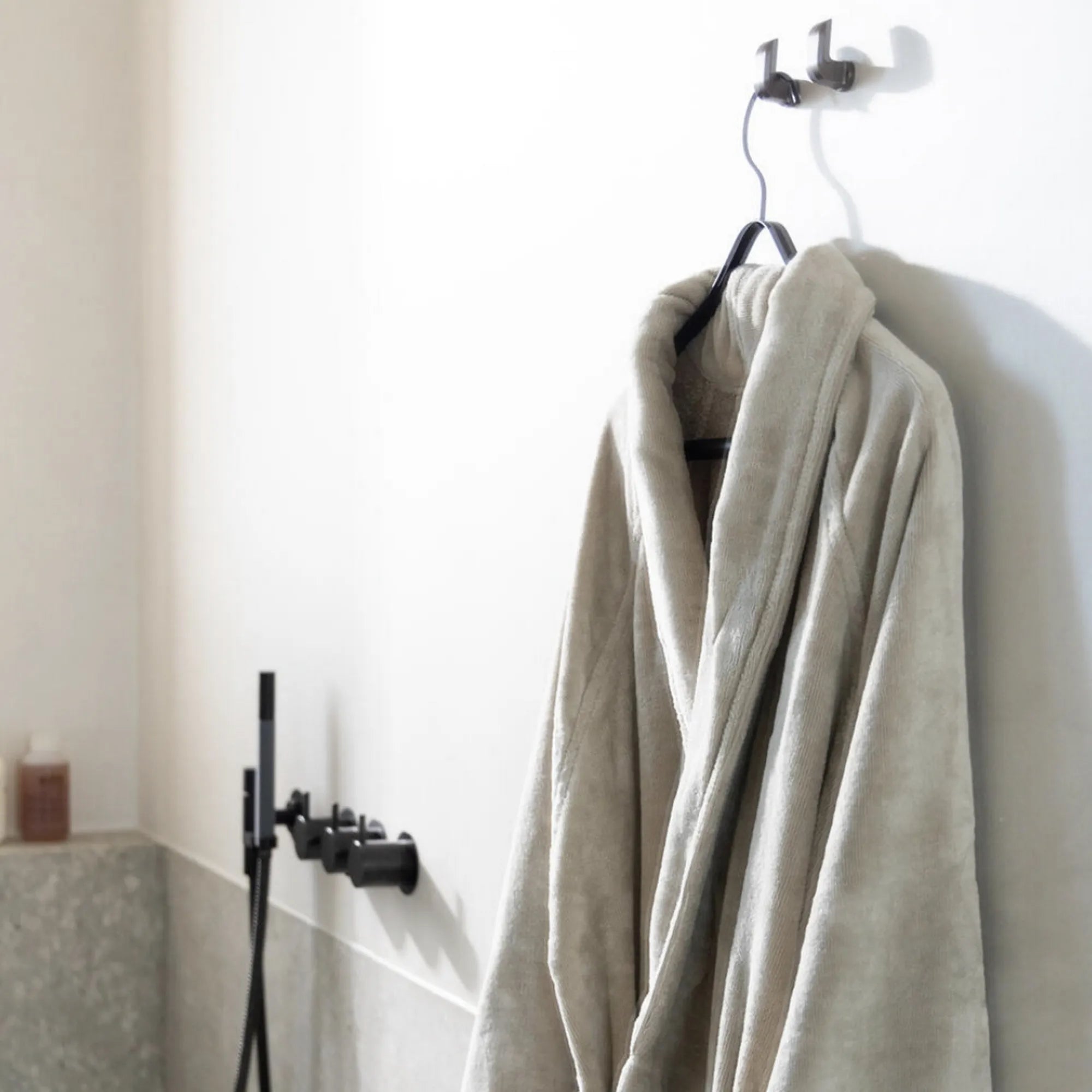 Luxe Flore badjas in greige, stijlvol gepresenteerd in een elegante badkamer. Gemaakt van 100% GOTS-gecertificeerd katoen met een zijdezachte buitenkant en absorberende binnenkant.