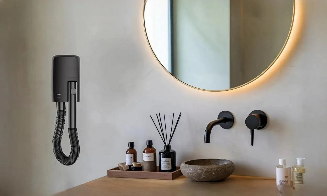 Zwarte wandhaardroger Hotello in badkamer met betonnen muur, naast spiegel met lichtrand, zwarte kranen en accessoires op het blad