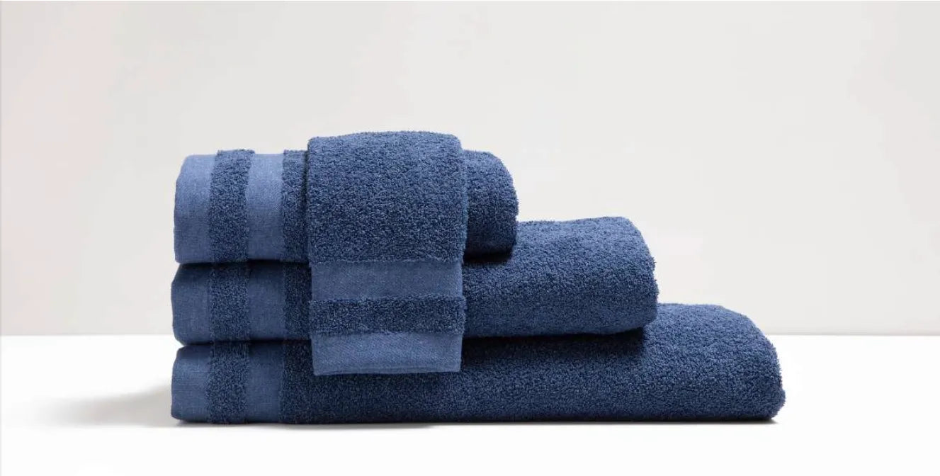 Set van vier indigoblauwe Luna-handdoeken, drie gevouwen op elkaar en een klein handdoekje dwars erbovenop, op witte en grijze achtergrond
