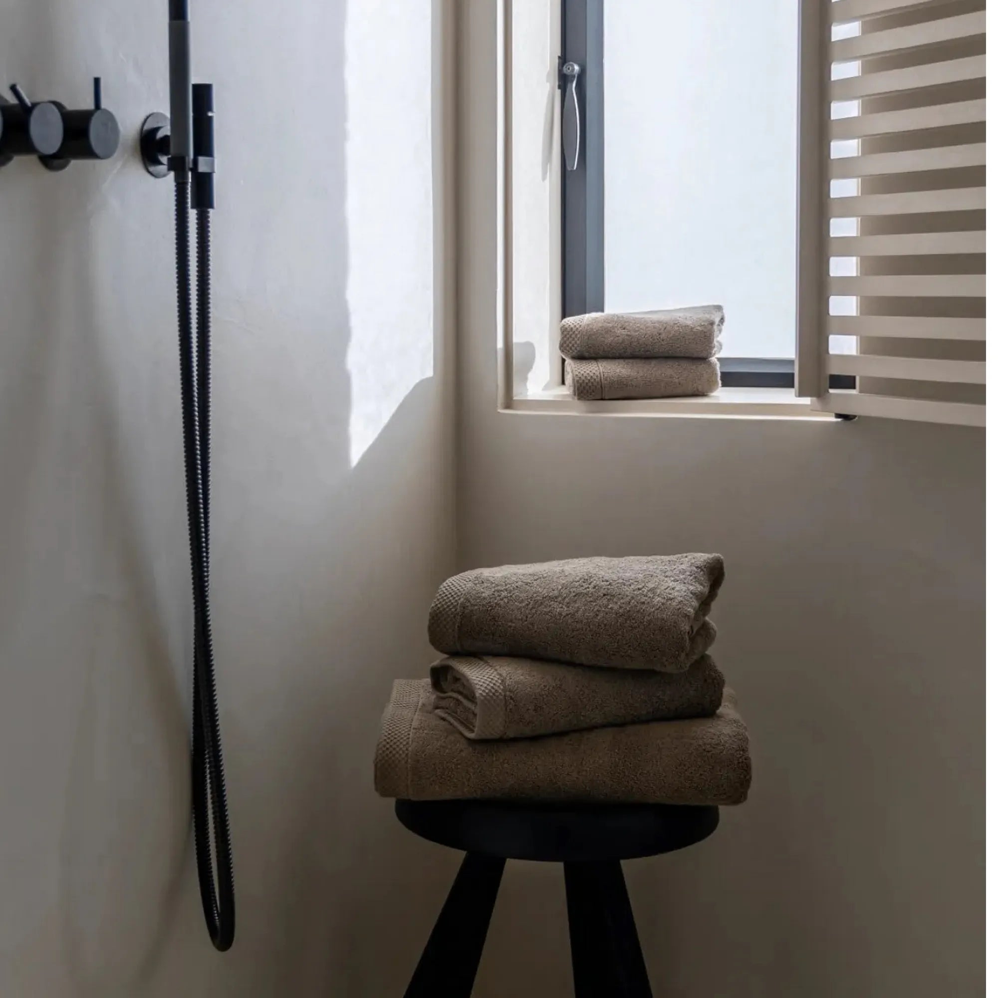 Vijf khaki handdoeken in luxe badkamer met betonlook, op houten krukje en bij het venster