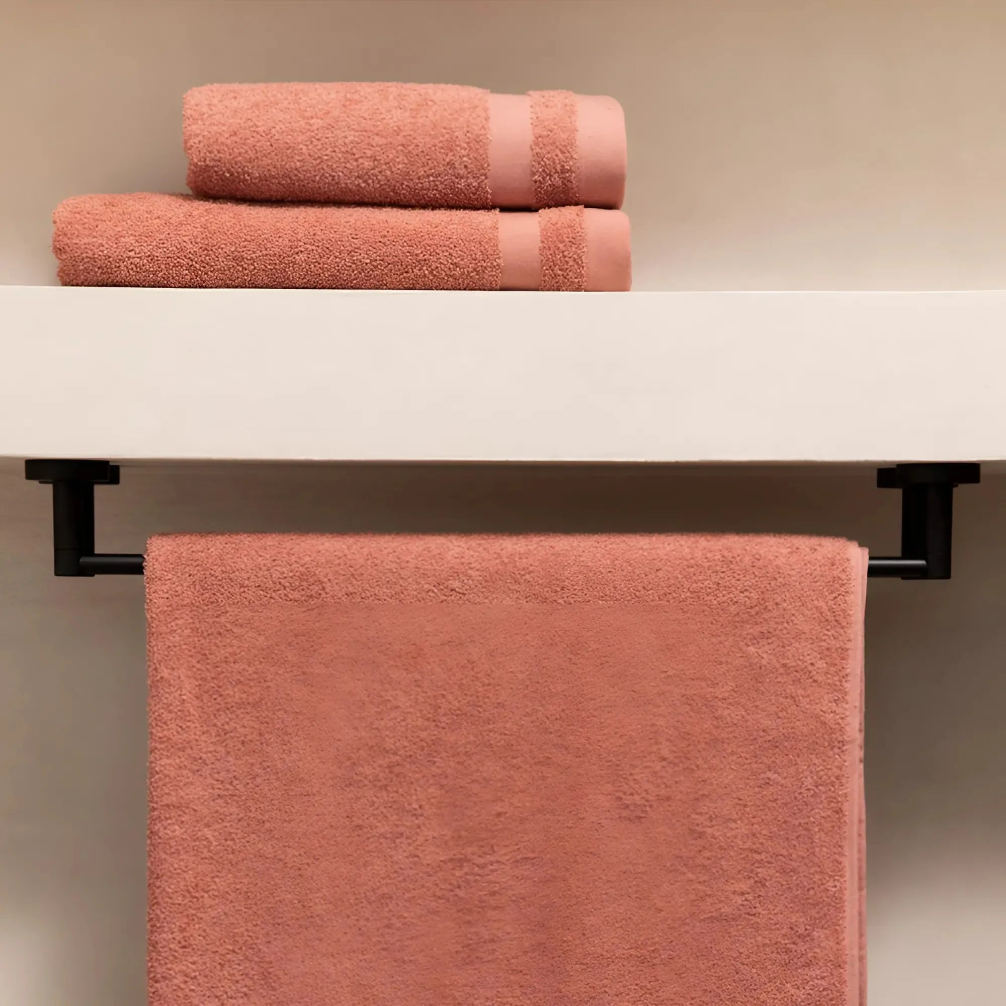 Roze Luna-handdoek over zwarte hanger, met kleinere gevouwen handdoeken op plank erboven in stijlvolle badkamer